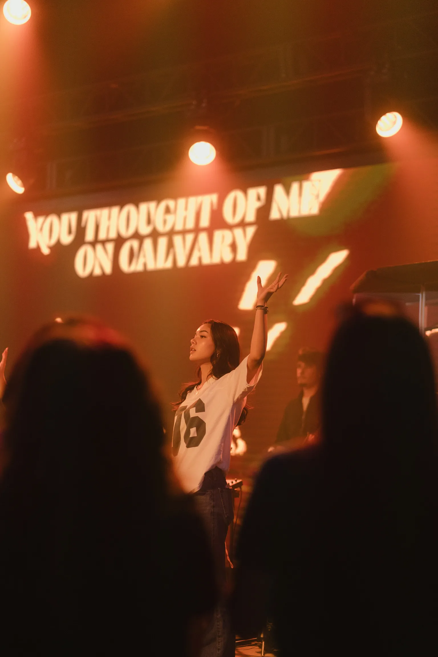 A student raises a hand in worship as stage lyrics read "you thought of me on Calvary"
