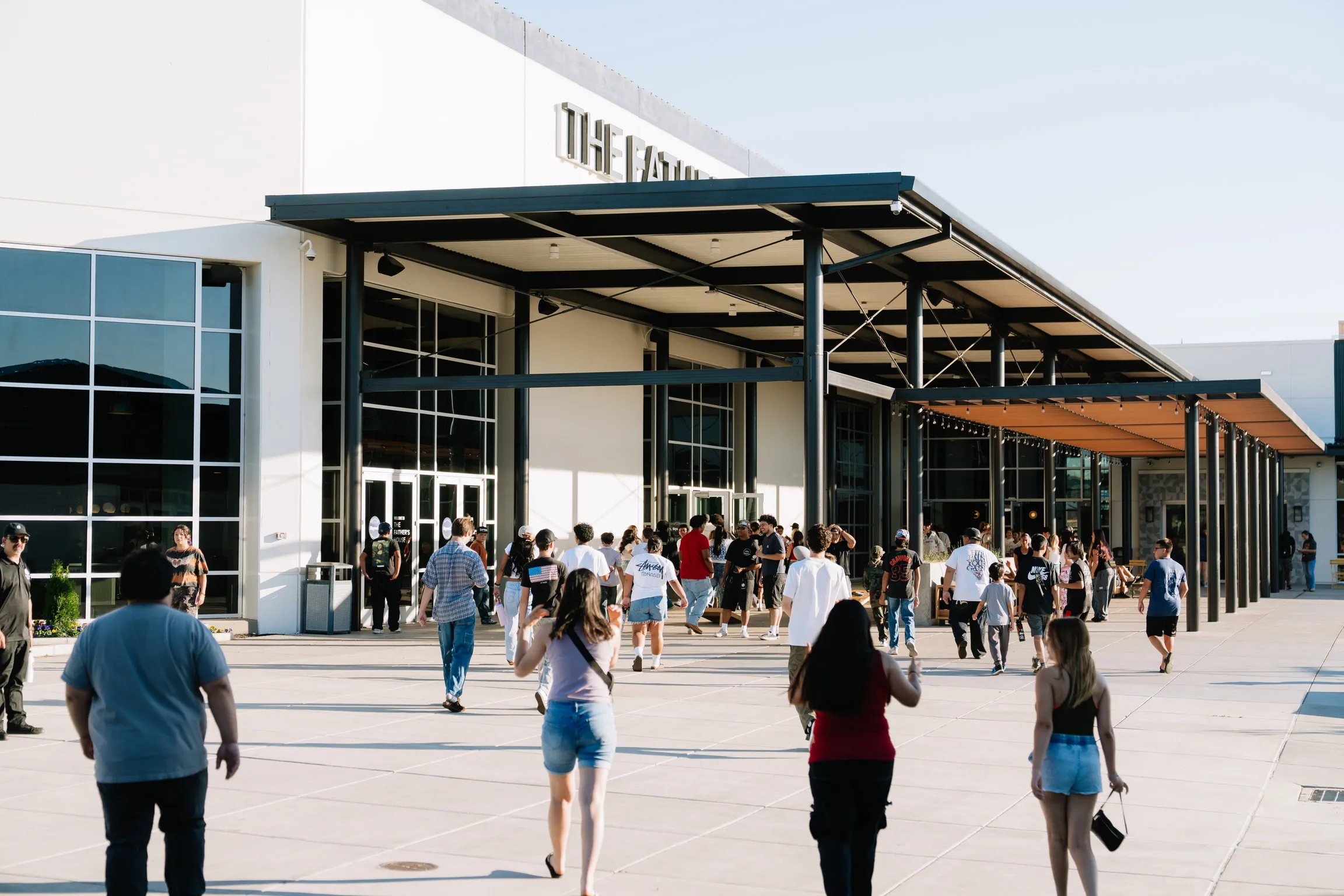 A crowd of students walks into the venue entrance on a sunny afternoon
