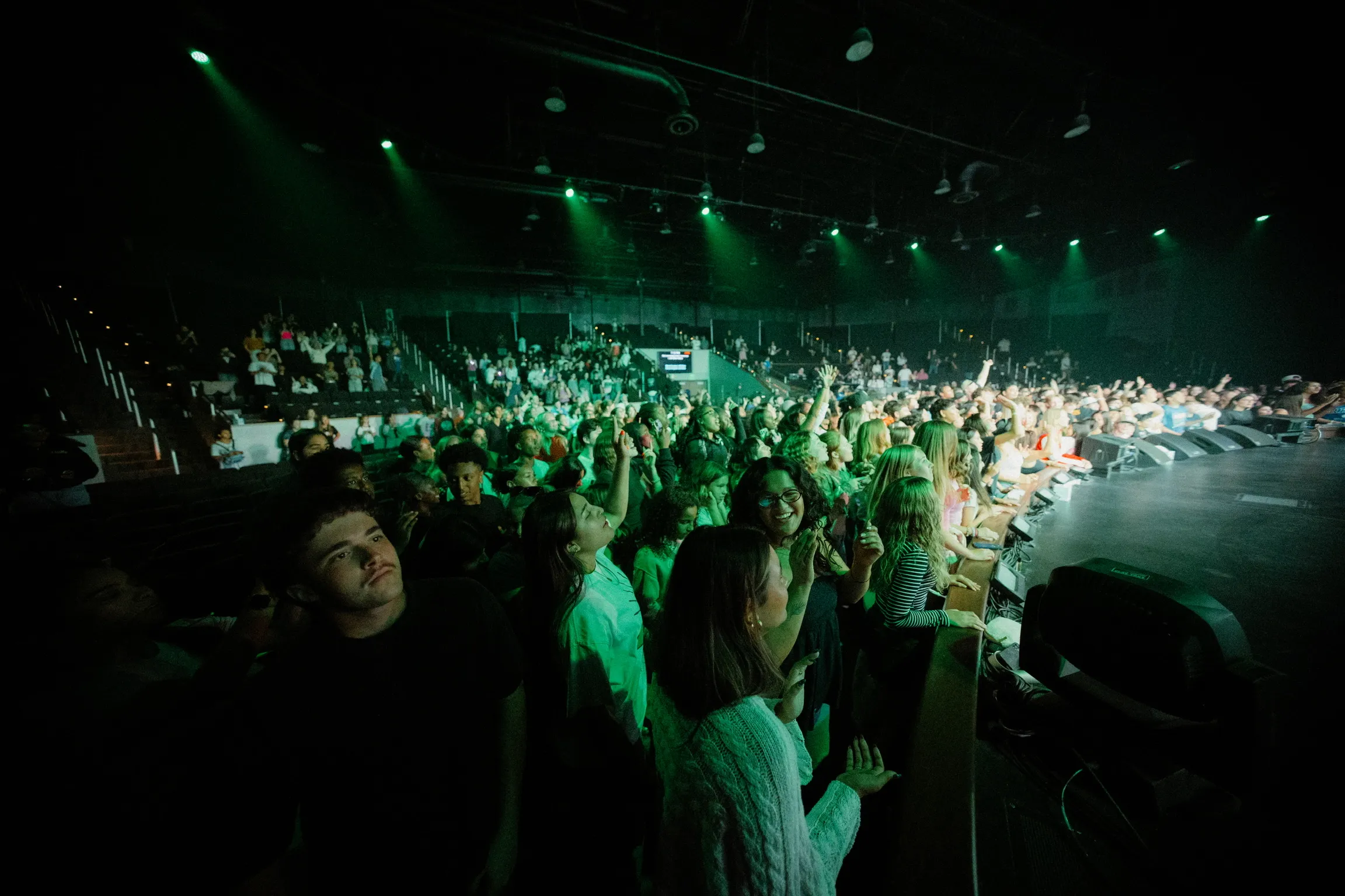 Wide view of a packed arena crowd lit in green stage light