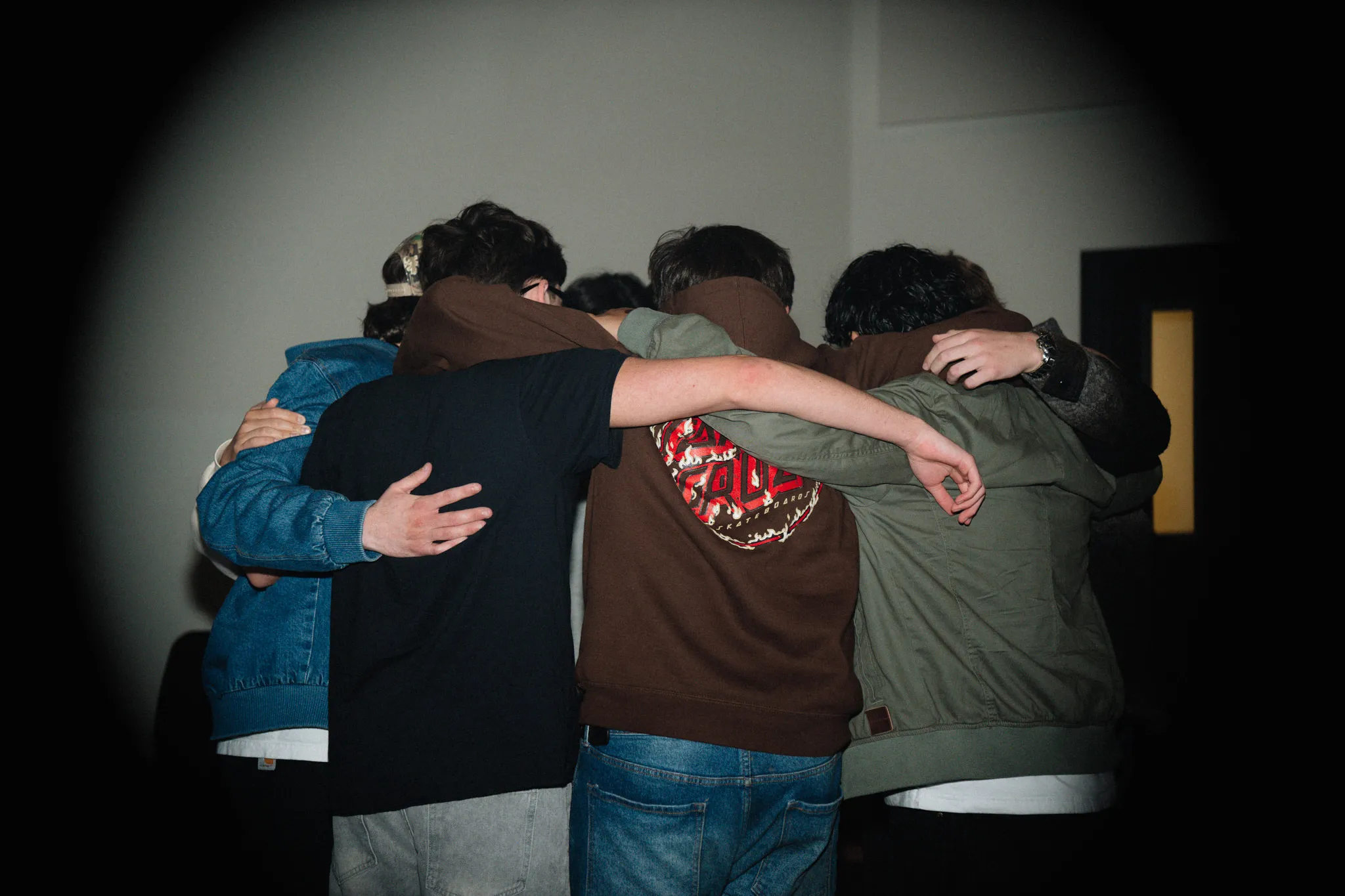 A group of friends stands with arms around each other's shoulders, backs to the camera