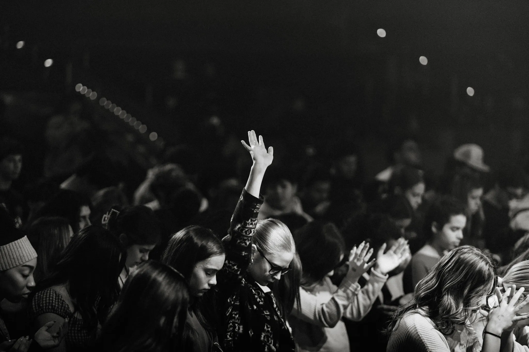 A black-and-white shot of a crowd worshiping with hands raised at night