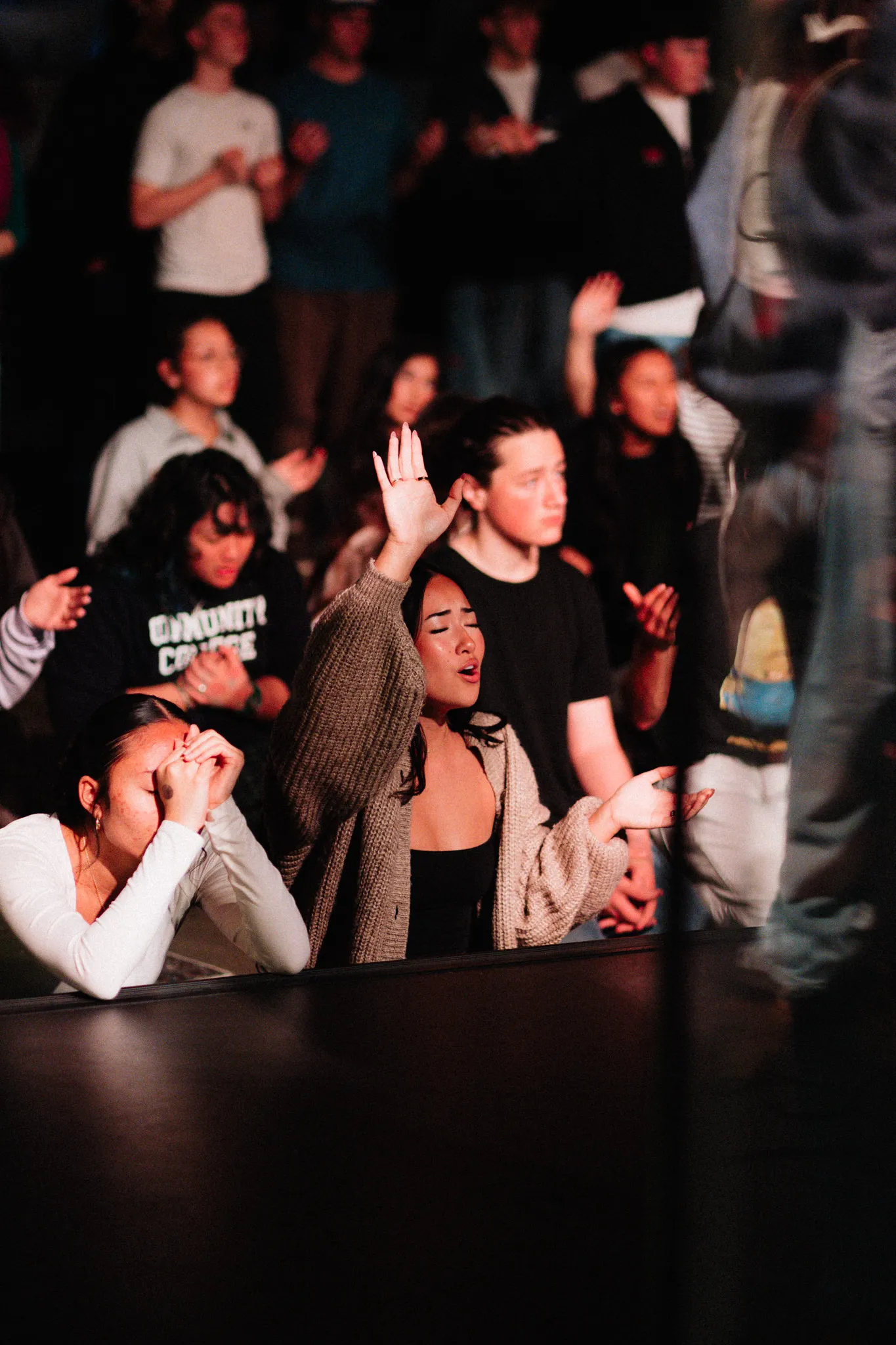 A woman raises a hand in worship, lit in red among a crowd at night
